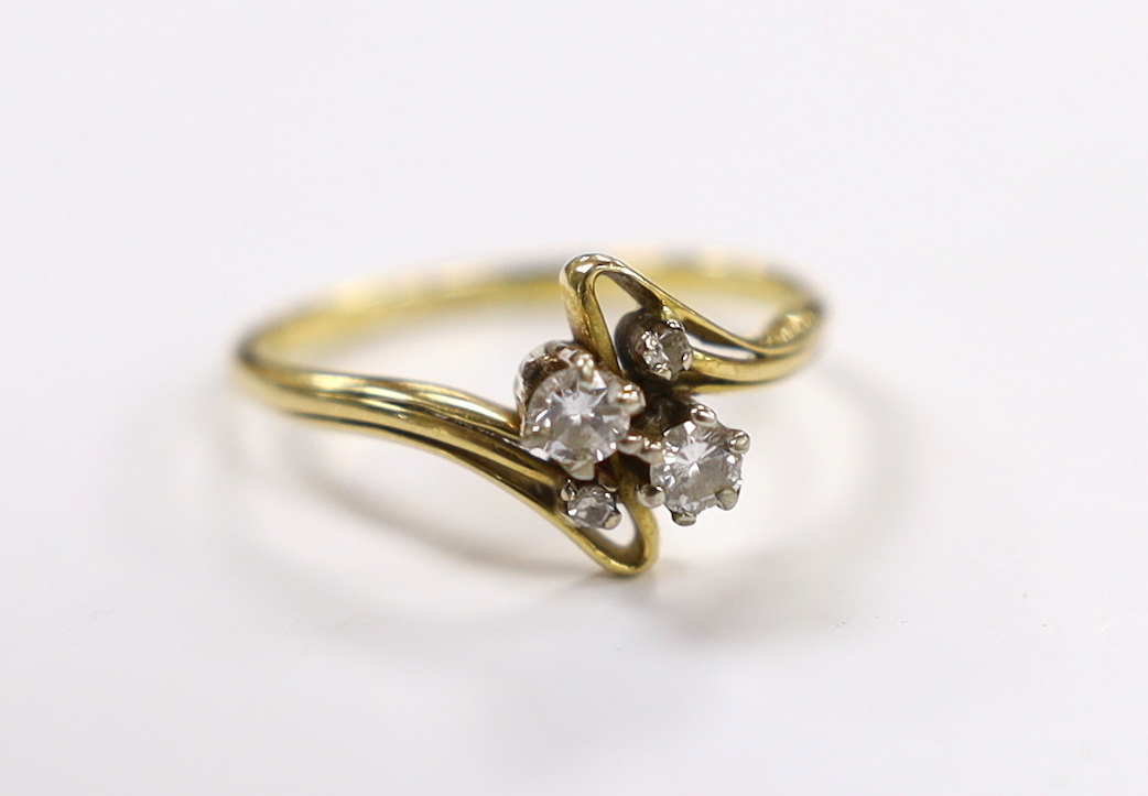 A yellow metal and graduated four stone diamond set crossover ring, size R, gross weight 3.4 grams.